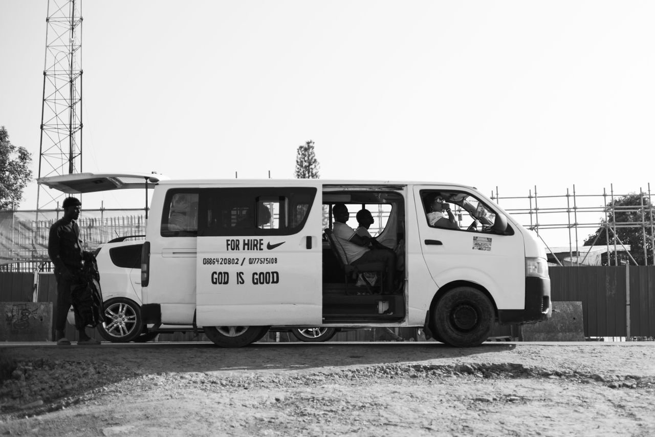 Street view of a minivan for hire with people inside in urban setting.