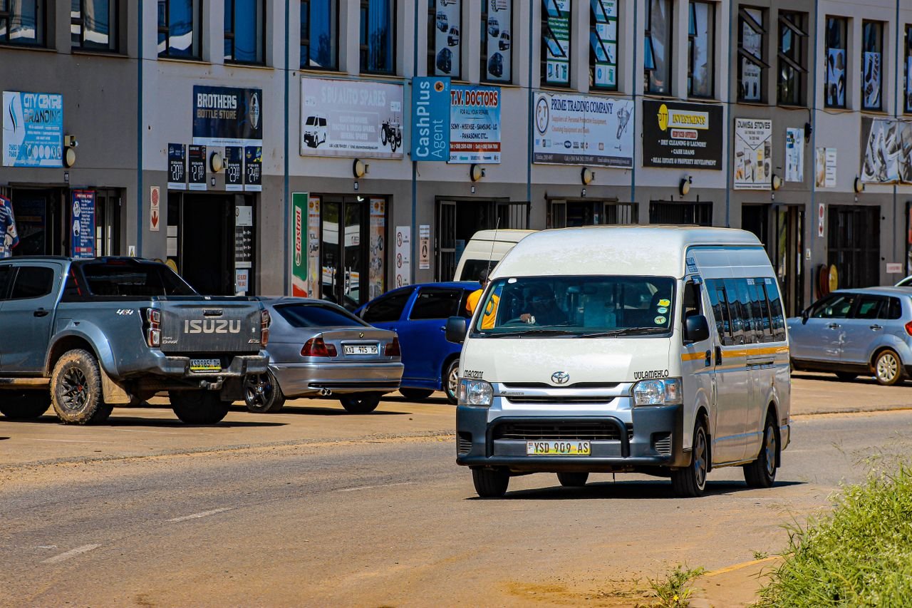 A busy street in an urban area with various cars and a white minibus taxi.