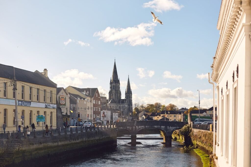 A beautiful scenic view of Cork City featuring a river, bridge, and cathedral on a sunny day.